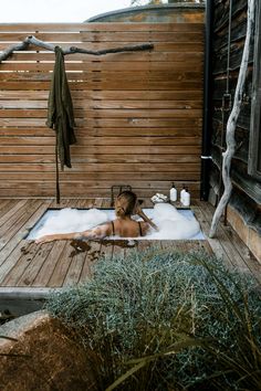 a woman laying in an outdoor hot tub surrounded by greenery and wooden fenced area