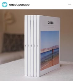 three books sitting on top of a white table next to a bed in a room