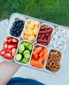 a person is holding a tray with fruits and pretzels in it that have words on them