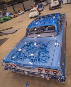 an old blue car is parked in a garage with other cars and people around it