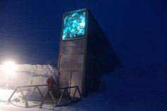 a person standing in the snow next to a building with a large screen on it's side