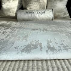 a close up of a bed with white and silver pillows on it's headboard