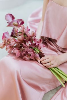 a woman in a pink dress holding a bouquet of purple orchids on her lap