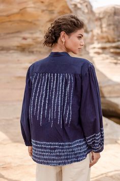 a woman standing in front of rocks wearing a blue shirt with white stripes on it