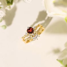 two gold rings with garnets and diamonds on them next to white flower petals