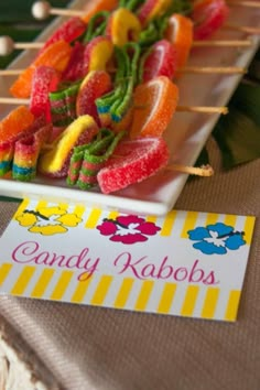 candy kabobs are arranged on a white plate with a yellow striped tablecloth