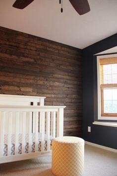 a white crib in front of a wooden wall with a window and ceiling fan