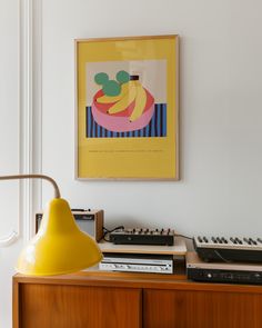 a yellow lamp sitting on top of a wooden dresser next to a painting and sound equipment