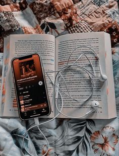 an open book with headphones on top of it next to a cell phone and earbuds