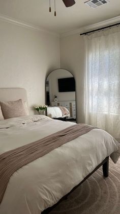 a bedroom with a bed, mirror and ceiling fan in the corner next to a window