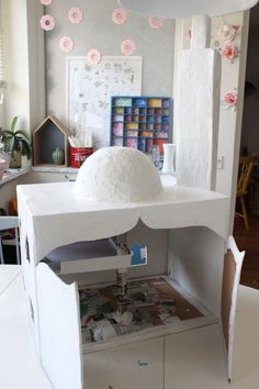 a doll house made out of cardboard and paper machs on the floor, with pink flowers hanging from the ceiling