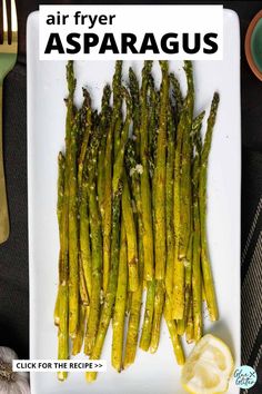 asparagus spears on a white plate with lemon wedges and fork next to it