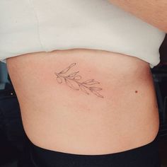 a woman's stomach with an olive branch tattoo on her side ribcage