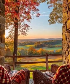 two wicker chairs sitting on top of a porch next to a stone wall and trees