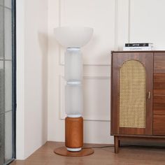 a white lamp sitting on top of a wooden floor next to a cabinet and door