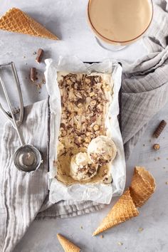 two scoops of ice cream sitting on top of a table next to cones and spoons