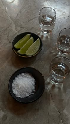 there are three glasses and two plates with limes on the table next to each other