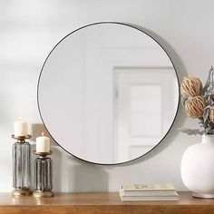 a round mirror sitting on top of a wooden table next to a vase with flowers