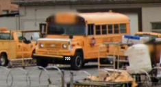 two yellow school buses parked next to each other in front of a building with barbed wire