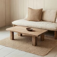 a wooden table sitting on top of a rug in front of a white couch next to a window