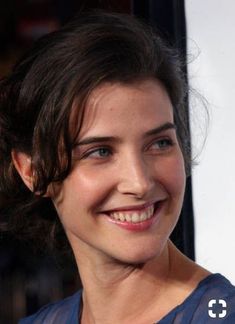 a close up of a person wearing a blue shirt and smiling at the camera with her hair pulled back