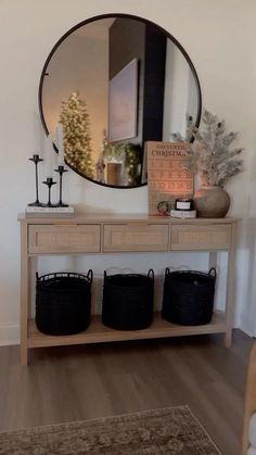 a wooden table with baskets under a round mirror on the wall next to a christmas tree