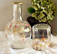 two glass vases sitting next to each other on a lace covered tablecloth with a potted plant in the background