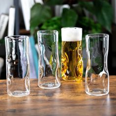 three glasses with different types of beer on a wooden table in front of a potted plant