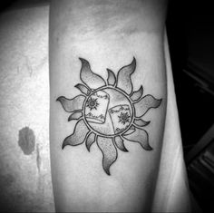 a black and white photo of a sun tattoo on the left arm with two symbols