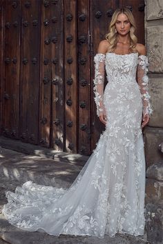 a woman in a white wedding dress standing next to a wooden door with her hands on her hips