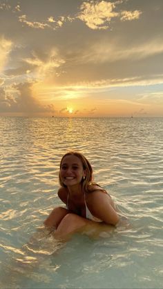 a woman is sitting in the water at sunset