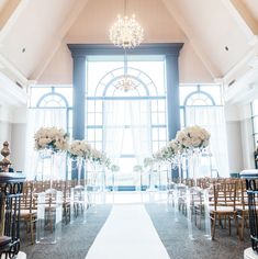 the aisle is lined with clear chairs and tall vases filled with flowers on each side