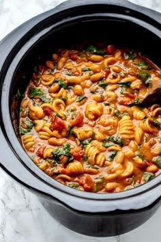 a pot filled with pasta and spinach on top of a marble countertop next to a wooden spoon