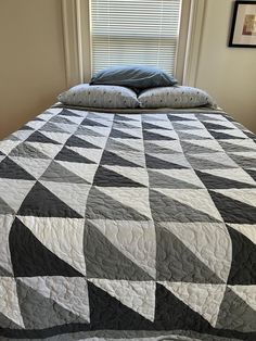 a bed with a black and white quilt on it's headboard next to a window