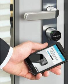 a hand holding a smart phone in front of an electronic door lock