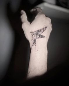 a small bird tattoo on the left wrist and right hand is shown in black and white