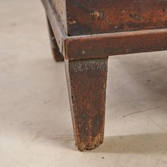 an old wooden bench sitting on top of a cement floor next to a white wall