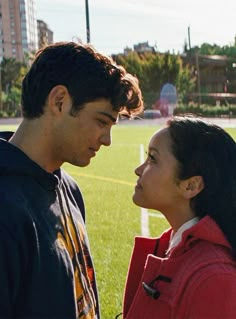 a man and woman standing next to each other in front of a soccer field on a sunny day