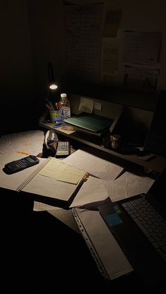 an office desk with notebooks, calculator and pen on it in the dark