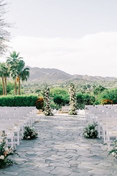 an outdoor ceremony with white chairs and greenery