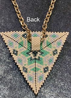 a gold chain necklace with a green and blue beaded triangle on the front, sitting on a gray surface