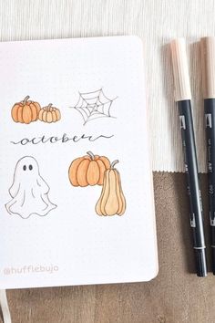 an open notebook with halloween drawings on it next to two markers and some pencils