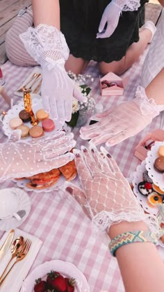 two women in white gloves are sitting at a table with food and plates on it