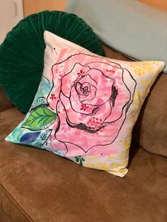 a pillow with a rose on it sitting on a couch next to a green pillow