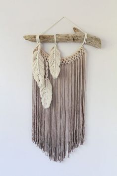 an image of a wall hanging made out of driftwood and some white feathers on it