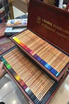 a wooden box filled with colored pencils on top of a table next to books