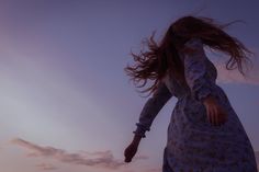 a woman is flying through the air with her hair blowing in the wind at sunset