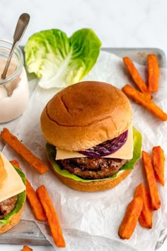 two hamburgers with lettuce, cheese and carrot fries on a tray next to a glass of milk