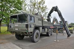 an army truck is parked on the side of the road with a crane attached to it