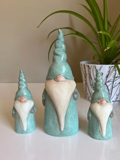 three ceramic gnomes sitting next to a potted plant